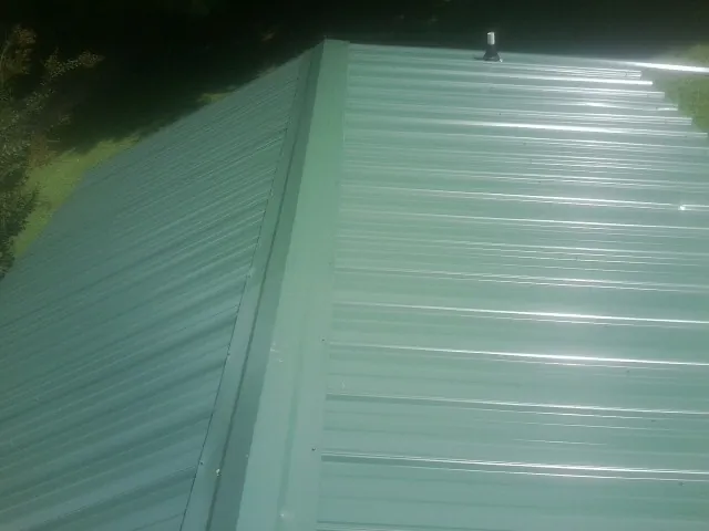 New green metal panels meeting at the ridge of a roof — Flat Roof Repair work by our crew in Dania